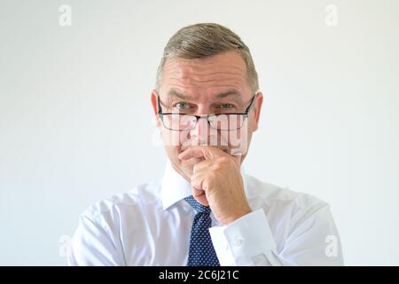 Homme attentif portant des lunettes droites avec une expression pensive et de la main au menton dans un portrait de la tête et des épaules Banque D'Images