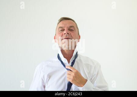 Un homme d'âge moyen perd sa cravate avec sa main dans un portrait frontal sur fond blanc Banque D'Images