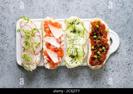 Sandwiches sur toasts avec des ingrédients simples, légumes, radis, tomates, concombres décorés de microverts sur gris. Vue de dessus. Banque D'Images