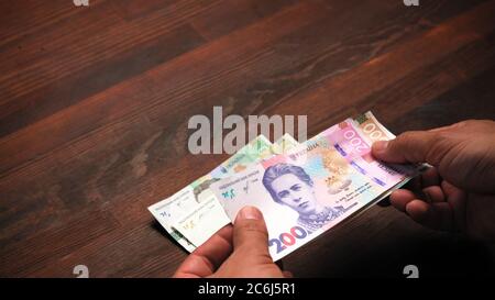 Les mains masculines comptent le papier-monnaie contenant des billets ukrainiens neufs, hryvnias sur une table en bois. Échange, concept. Gros plan Banque D'Images