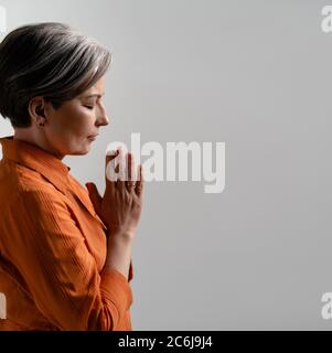 La femme spirituelle caucasienne prie avec ses mains jointes. Vue latérale d'une femme mûre méditant avec les yeux fermés. Forme carrée avec espace de copie pour les réseaux sociaux Banque D'Images