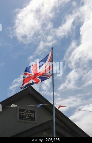 Broomhaie, Comté d'Antrim, Irlande du Nord. 10 juillet 2020. Météo britannique – averses légères mais fréquentes et soleil dus à une brise du nord-ouest. Une salle orange rurale en Irlande du Nord avec drapeau Union Jack volant à côté de rouge blanc et bleu bunting au soleil. En raison de Covid 19 il n'y aura pas de manifestations annuelles du 12 juillet par des pavillons orange dans quelques jours, mais les bandes peuvent décider de défilé - la commission des parades a vu plus de 200 demandes dans les derniers jours . Crédit : CAZIMB/Alamy Live News. Banque D'Images