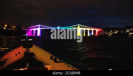 Bangor, Gwynedd, N pays de Galles. Suspension de Menai le pont au-dessus du détroit de Menai est illuminé dans des couleurs arc-en-ciel pour célébrer 72 ans du NHS Banque D'Images