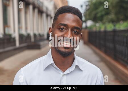 Portrait d'un homme d'affaires noir souriant avec des écouteurs sans fil à l'extérieur Banque D'Images