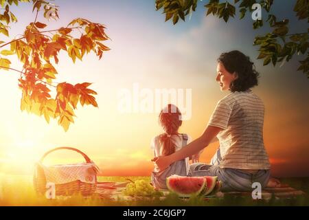 Pique-nique en famille. La jeune mère et sa fille enfant profitent d'un repas sain en plein air assis ensemble sur l'herbe verte dans le parc d'été.