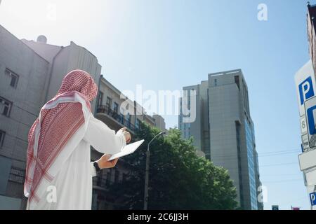 Riche portrait d'homme arabe lors de l'achat de biens immobiliers, centre d'affaires en ville. Ethnicité, culture, inclusion. Homme d'affaires confiant dans les vêtements traditionnels faisant une affaire réussie. Finances, économie. Banque D'Images