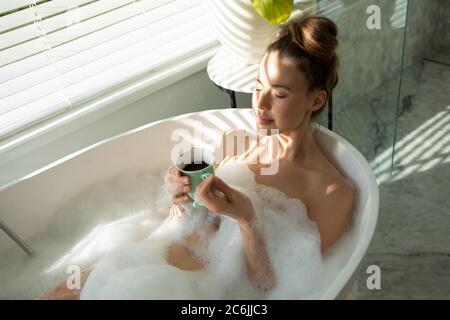 Femme avec une tasse de café se détendre dans une baignoire Banque D'Images