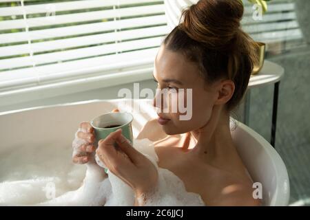 Femme avec une tasse de café se détendre dans une baignoire Banque D'Images