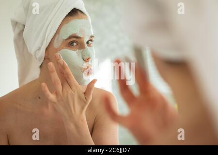 Femme appliquant le paquet de visage en regardant dans le miroir Banque D'Images