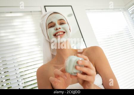 Femme appliquant le paquet de visage en regardant dans le miroir Banque D'Images