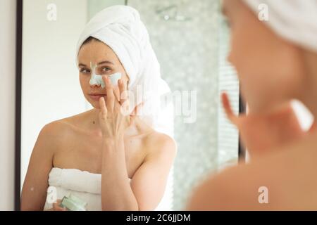Femme appliquant le paquet de visage en regardant dans le miroir Banque D'Images
