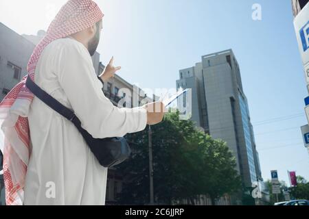 Contrat. Riche portrait d'homme arabe lors de l'achat de biens immobiliers, centre d'affaires en ville. Ethnicité, culture. Homme confiant dans les vêtements traditionnels faisant une affaire réussie. Finances, économie. Banque D'Images