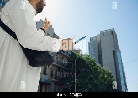 Contrat. Riche portrait d'homme arabe lors de l'achat de biens immobiliers, centre d'affaires en ville. Ethnicité, culture. Homme confiant dans les vêtements traditionnels faisant une affaire réussie. Finances, économie. Banque D'Images