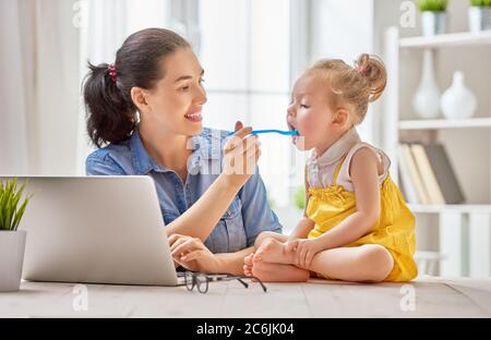 Jeune mère avec enfant en bas âge travaillant sur l'ordinateur à la maison. Banque D'Images