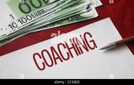 Mot de coaching sur page, stylo et 100 euros de factures. Concept de conseil en affaires de la vie Banque D'Images