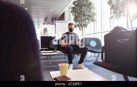 Un homme attendant dans un aéroport vide portant un masque facial de protection utilisant la technologie. Banque D'Images