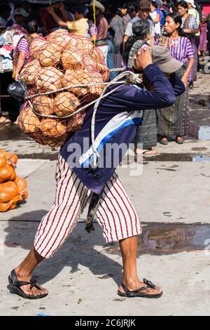 Guatemala, Département de Solola, Santiago Atitlan, UN jeune homme porte une lourde charge d'oranges du marché sur son dos en utilisant une ligne de ventre. Banque D'Images