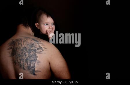 Portrait de bébé mignon avec le symbole Heavy Metal et Hard Rock - main de corne sur fond noir. Un papa tatoué embrasse et tient son bébé. Amour et soin Banque D'Images