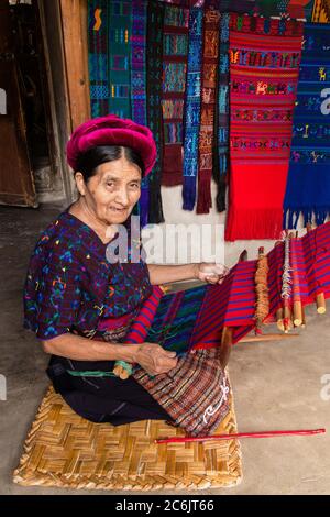 Guatemala, département de Solola, Santa Catarina Palopo, une ancienne femme maya Cakchiquel se déchèle du tissu sur une toile de toile de fond tout en s'agenouillant sur le sol de sa maison. Banque D'Images