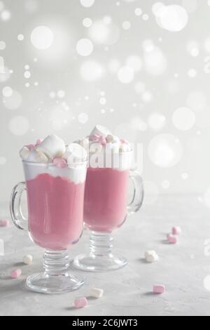 Chocolat chaud au rubis rose avec crème fouettée et bonbons guimauve dans 2 tasses en verre. Ambiance de Noël. Espace de copie, vertical. Banque D'Images