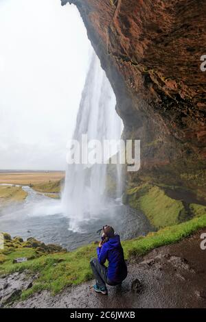 Photos de visiteurs Seljalandsfoss, une cascade spectaculaire qui tombe à 213 mètres (65 pieds) sur une vieille falaise. Il est juste à côté du périphérique dans le sud de l'Islande. Un court chemin mène les gens derrière l'eau qui tombe. Banque D'Images