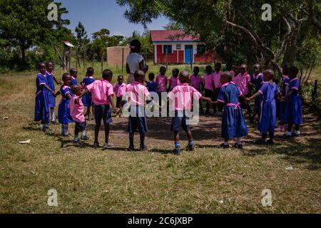Les enfants des écoles tiennent les mains et forment un cercle autour de leur professeur lorsqu'ils jouent à l'ombre pour échapper au soleil africain Banque D'Images