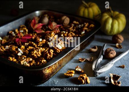 Noix entières et coupées en deux dans une casserole avec casse-noisette et citrouilles sur fond sombre. Banque D'Images