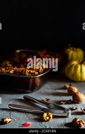 Noix entières et coupées en deux dans une casserole avec casse-noisette et citrouilles sur fond sombre. Espace de copie, vertical Banque D'Images