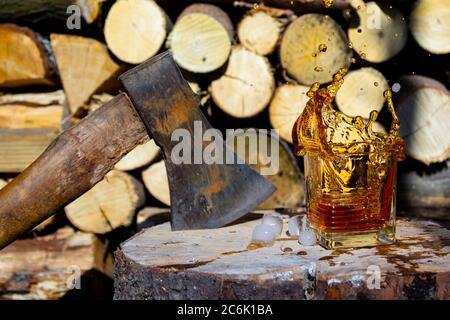 Verre de whisky scotch avec glaçons et éclaboussures sur fond de bois. Concept brutal avec hache, lumière naturelle Banque D'Images