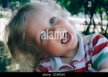 Portrait d'un joli petit garçon heureux avec des cheveux blonds et des yeux bleus, en train de faire un chapeau, de sourire et de jouer dans le parc. Retour au concept normal. Banque D'Images