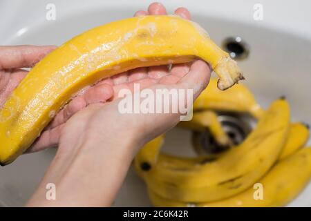 La fille lave les bananes avec du savon. Mains et bananes savonnelles dans l'évier. Banque D'Images