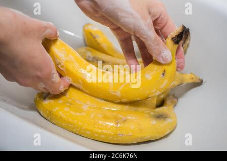 La fille lave les bananes avec du savon. Mains et bananes savonnelles dans l'évier. Banque D'Images