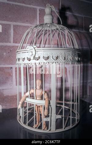 Mannequin humain en bois verrouillé à l'intérieur d'une cage d'oiseau ornemental blanc Banque D'Images