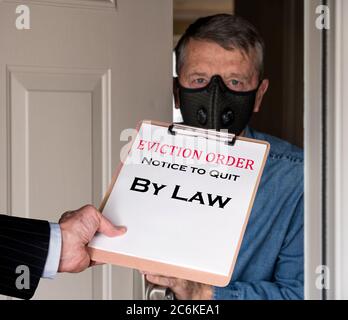 Ouvrez la porte avant avec un homme en costume donnant un avis d'expulsion à un locataire défaillant avec masque facial pendant l'épidémie de coronavirus Banque D'Images