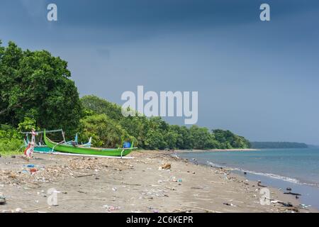 vieux bateau en bois vert sur une plage tropicale. bateau balinais typique. pile de déchets déversés par la mer Banque D'Images