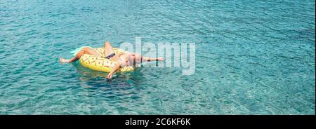 Homme se détendant en nageant sur un anneau gonflable de piscine d'ananas dans l'eau de mer cristalline. Image de concept de vacances imprudente. Banque D'Images
