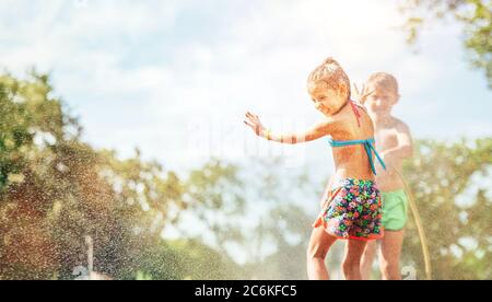 Deux enfants jouent avec l'eau saupoudrée dans le jardin d'été Banque D'Images