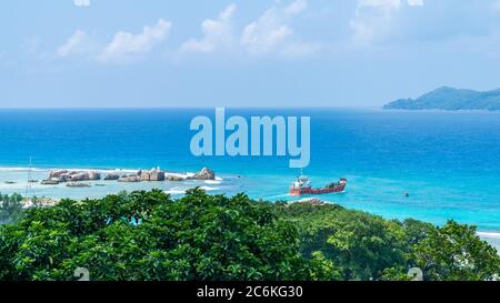 Vue panoramique sur les célèbres rochers de granit dans la mer bleue à la Digue, Seychelles. Navire de cargaison orange allant à l'île de Praslin Banque D'Images