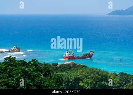 Vue panoramique sur les célèbres rochers de granit dans la mer bleue à la Digue, Seychelles. Navire de cargaison orange allant à l'île de Praslin Banque D'Images