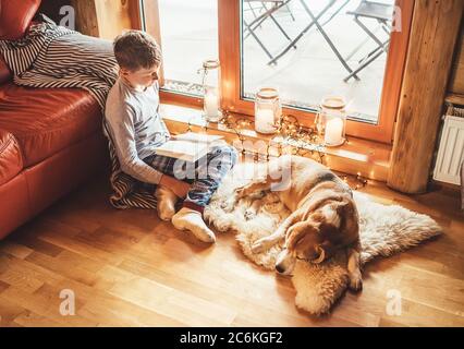 Garçon lisant le livre sur le sol près de glisser son chien de beagle sur peau de mouton dans une atmosphère confortable de maison. Un concept de maison confortable pour des moments paisibles. Banque D'Images