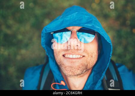 Backpacker homme a une pause de repos appréciant la montagne de marche pause, il a levé sa tête dans l'air. Il porte un poncho imperméable bleu et des lunettes de soleil bleues. A Banque D'Images