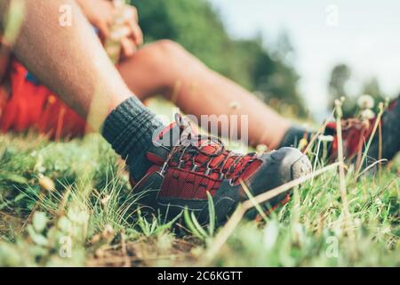Chaussures de randonnée Backpacker gros plan. L'homme a une pause de repos assis sur l'herbe verte et appréciant la randonnée de montagne, sport actif Backpacking santé Banque D'Images