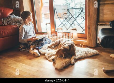 Garçon lisant le livre sur le sol près de glisser son chien de beagle sur peau de mouton dans une atmosphère confortable de maison. Un concept de maison confortable pour des moments paisibles. Banque D'Images