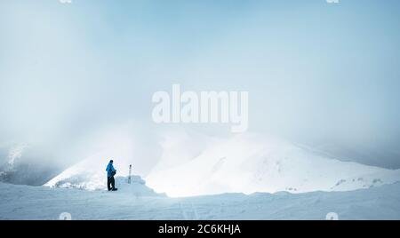 Trekker d'hiver restant sur le sommet de la montagne il a grimpé et enjojing large vue panoramique de la vallée couverte par les nuages de tempête. Trekking d'hiver actif concept i Banque D'Images