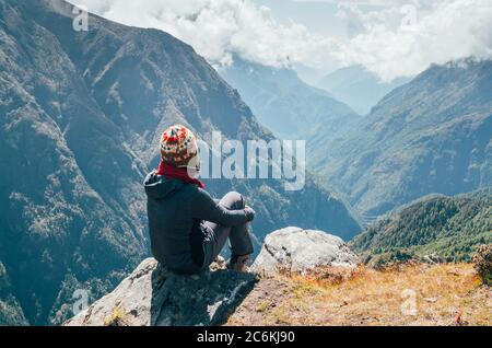 Jeune randonneur assis sur le bord de crête et appréciant la vue sur les montagnes vallée pendant la haute altitude Everest base Camp (EBC) randonnée route près de pH Banque D'Images