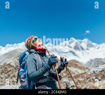 Une jeune randonneur prend le frein lors d'une randonnée pédestre pendant la route de l'Everest base Camp (EBC) en haute altitude avec des sommets de l'Himalaya enneigés en arrière-plan. Banque D'Images