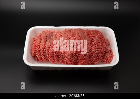 Viande hachée (hachée) brute dans un contenant en mousse de polystyrène blanc isolé sur fond noir avec espace de copie pour le texte Banque D'Images