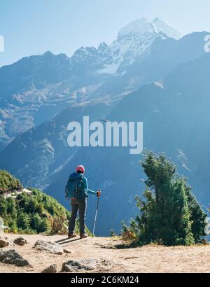 Jeune randonneur utilisant des bâtons de randonnée appréciant la montagne Thamserku 6608m avec vol de sauvetage hélicoptère pendant haute altitude Acclimatiza Banque D'Images