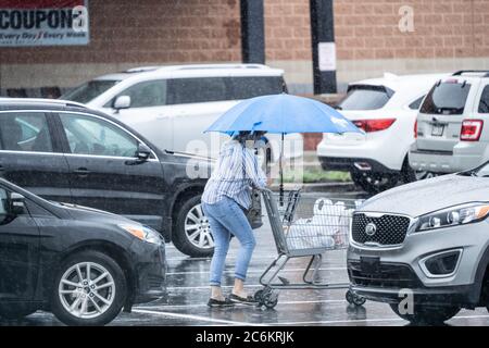 Les femmes âgées poussent l'épicerie dans le stationnement sous la pluie. Banque D'Images