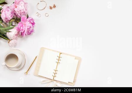 Un bouquet de pivoines roses, un stylo doré, des bijoux pour femmes et un journal sur fond blanc. Café dans une tasse blanche. Copier l'espace. Banque D'Images